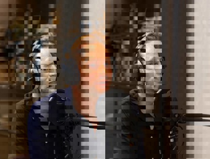 Een man met een hoofdtelefoon zit achter een microfoon in een sfeervolle studio.