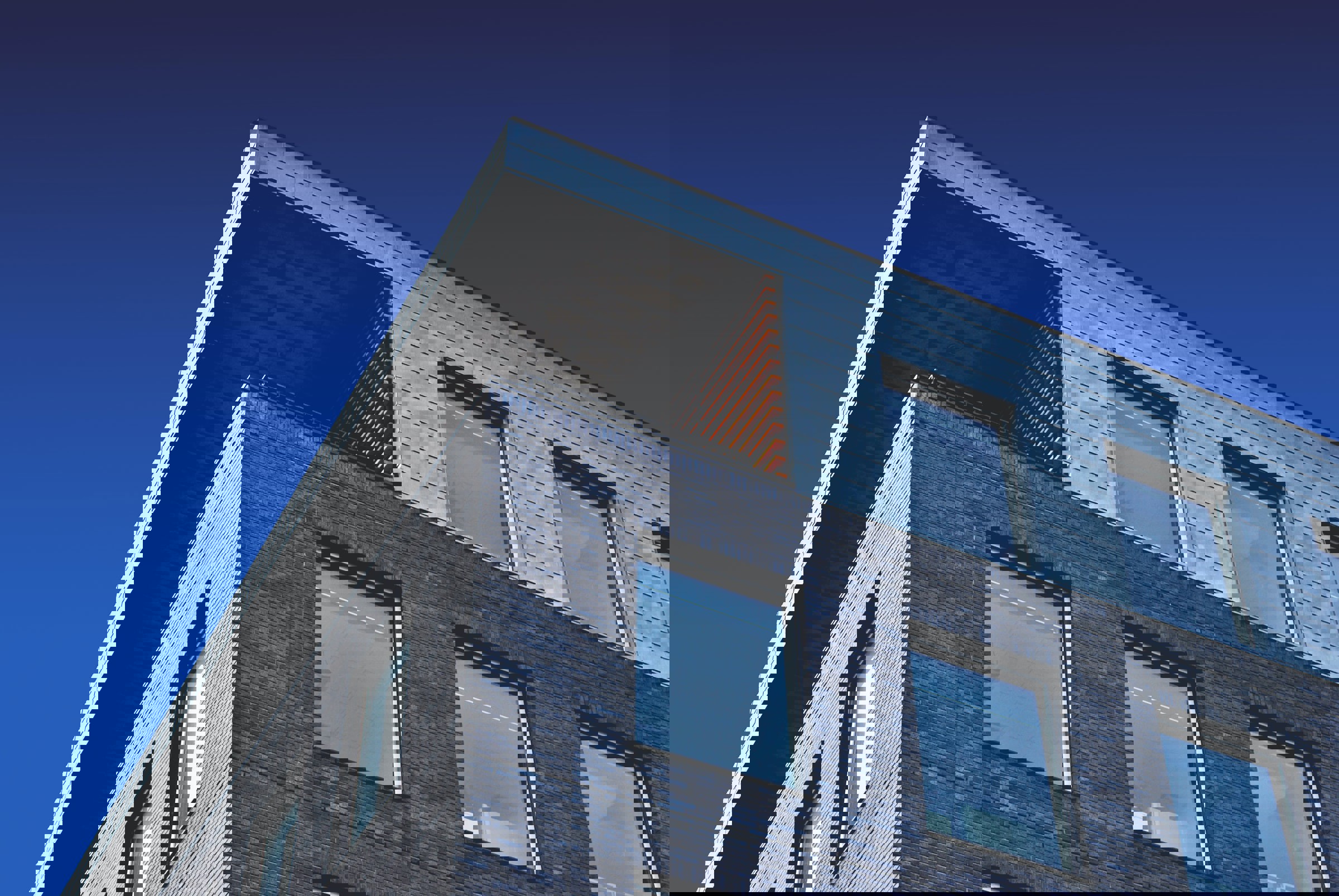 Modern gebouw met een metalen dak en een bakstenen gevel, tegen een achtergrond van een blauwe lucht.