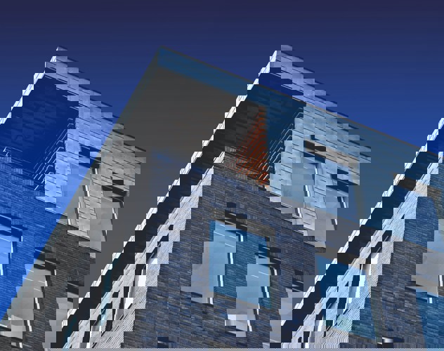 Modern gebouw met een metalen dak en een bakstenen gevel, tegen een achtergrond van een blauwe lucht.