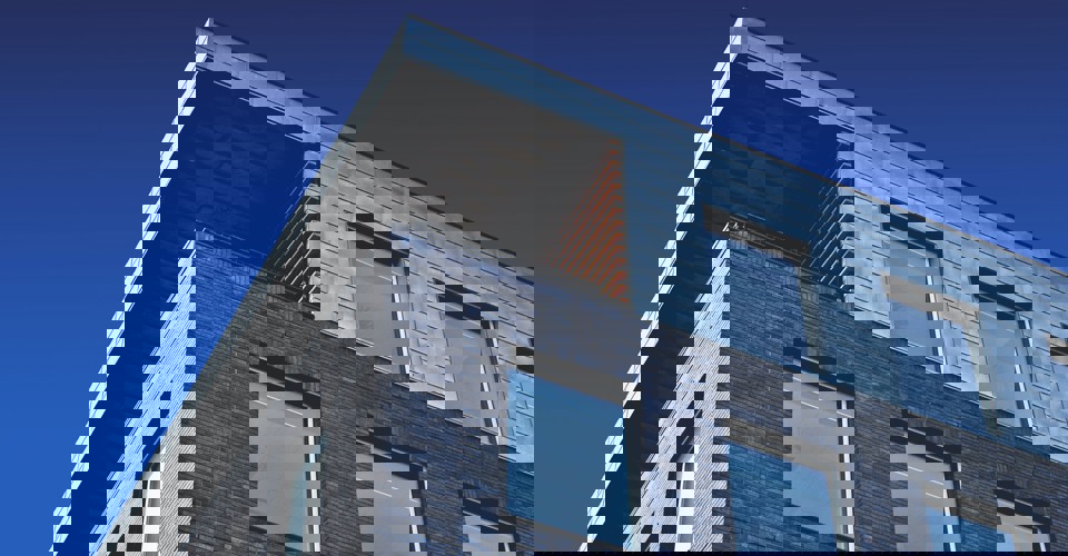 Modern gebouw met een metalen dak en een bakstenen gevel, tegen een achtergrond van een blauwe lucht.