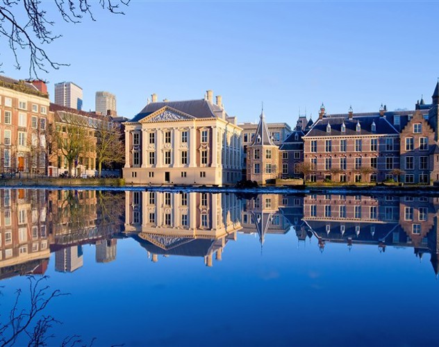 Historisch gebouw aan de Haagse Hofvijver met reflectie in het water, omringd door moderne en traditionele architectuur.