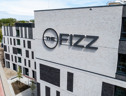 The Fizz building featuring modern architecture and a prominent name on the facade, surrounded by green landscaping and a sidewalk.