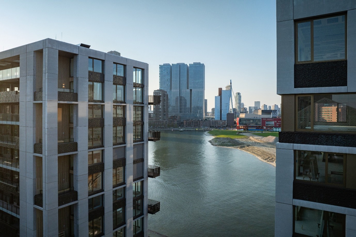 View of modern buildings along a river, with a city skyline in the background.
