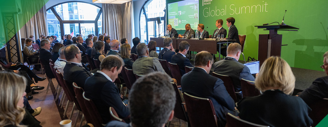 Panel discussion at a conference with speakers at a podium and an audience listening attentively.