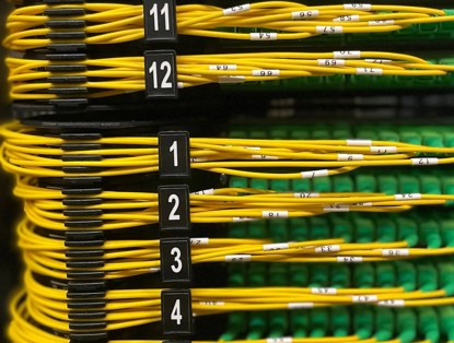 Geordende gele netwerkkabels met genummerde etiketten, bevestigd aan een apparatuurrek, voor een gestructureerde dataverbinding.