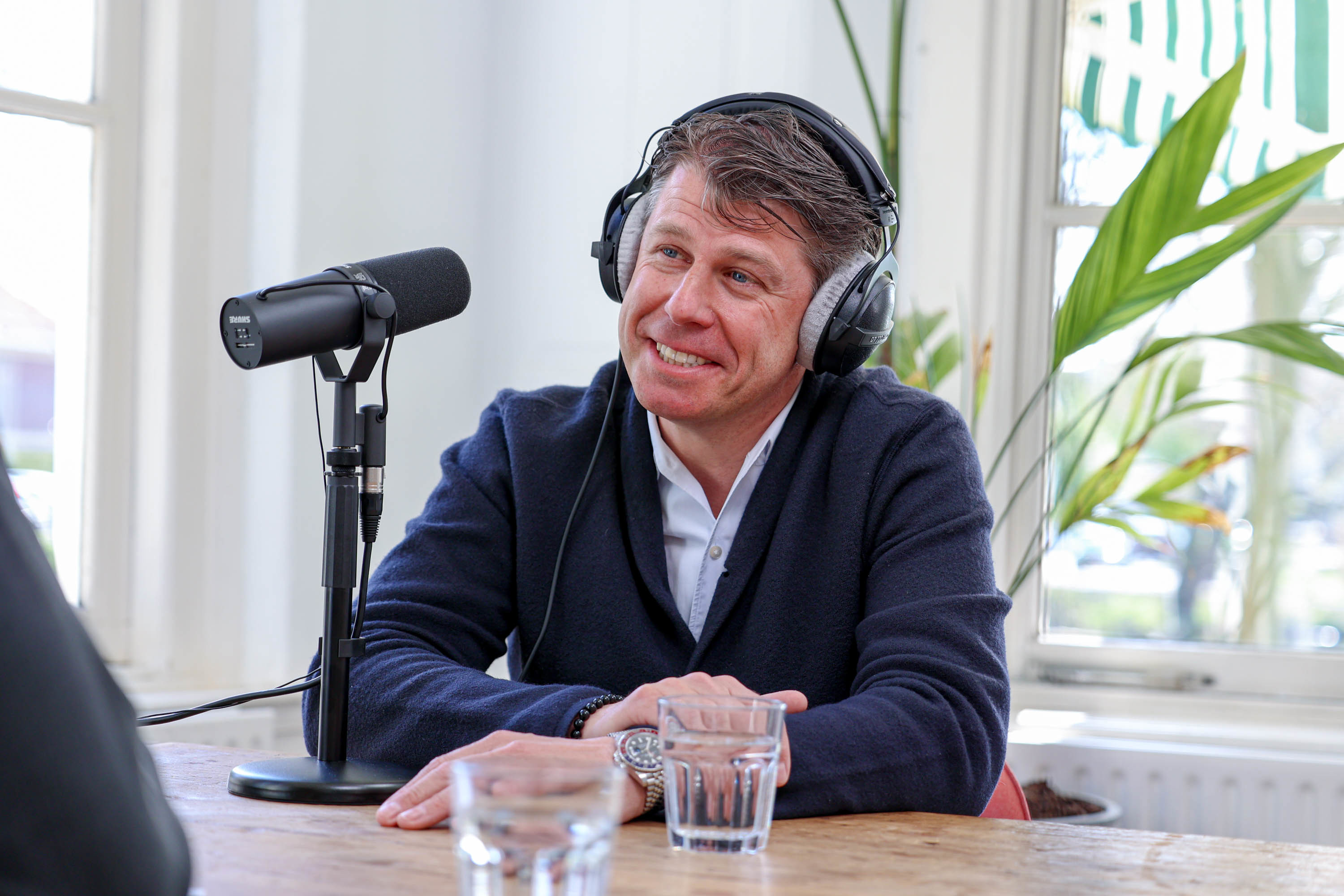 Een persoon met een hoofdtelefoon zit aan een tafel met een microfoon en bereidt zich voor op een gesprek.