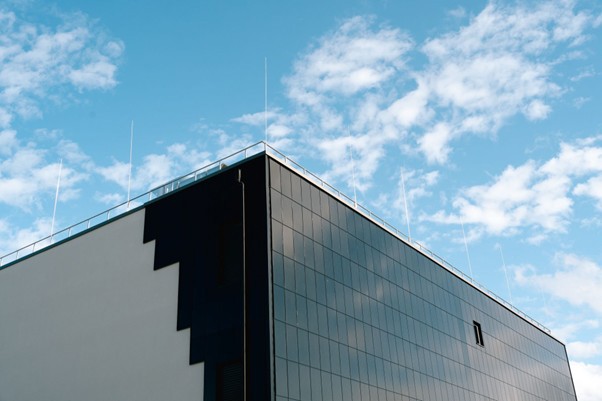Corner of a modern building with a reflective black facade against a bright blue sky with light clouds.