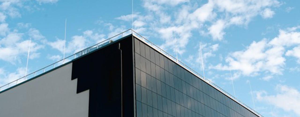 Corner of a modern building with a reflective black facade against a bright blue sky with light clouds.