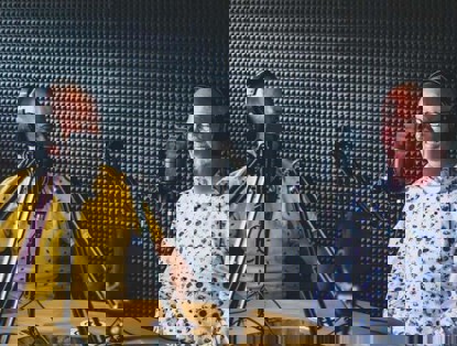 Twee mannen zitten aan een tafel in een opnamestudio, met een microfoon voor zich en een koptelefoon op.