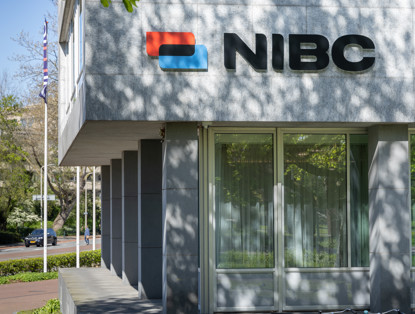 NIBC office with a red and blue logo on a modern facade, surrounded by green trees.