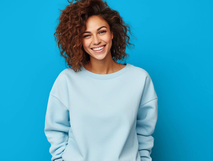 Vrouw met een vol, krullend kapsel in een lichtblauwe trui, voor een felle blauwe achtergrond.