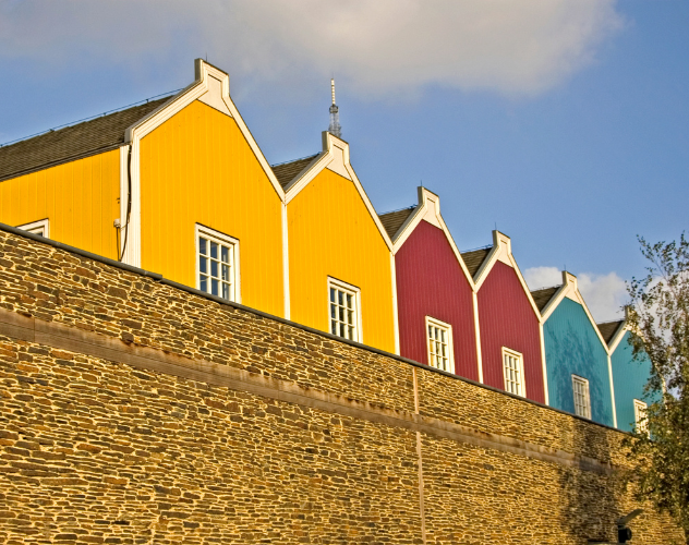 Vrolijke gekleurde gevels in geel, rood en blauw, met een stenen muur eronder, tegen een heldere lucht.