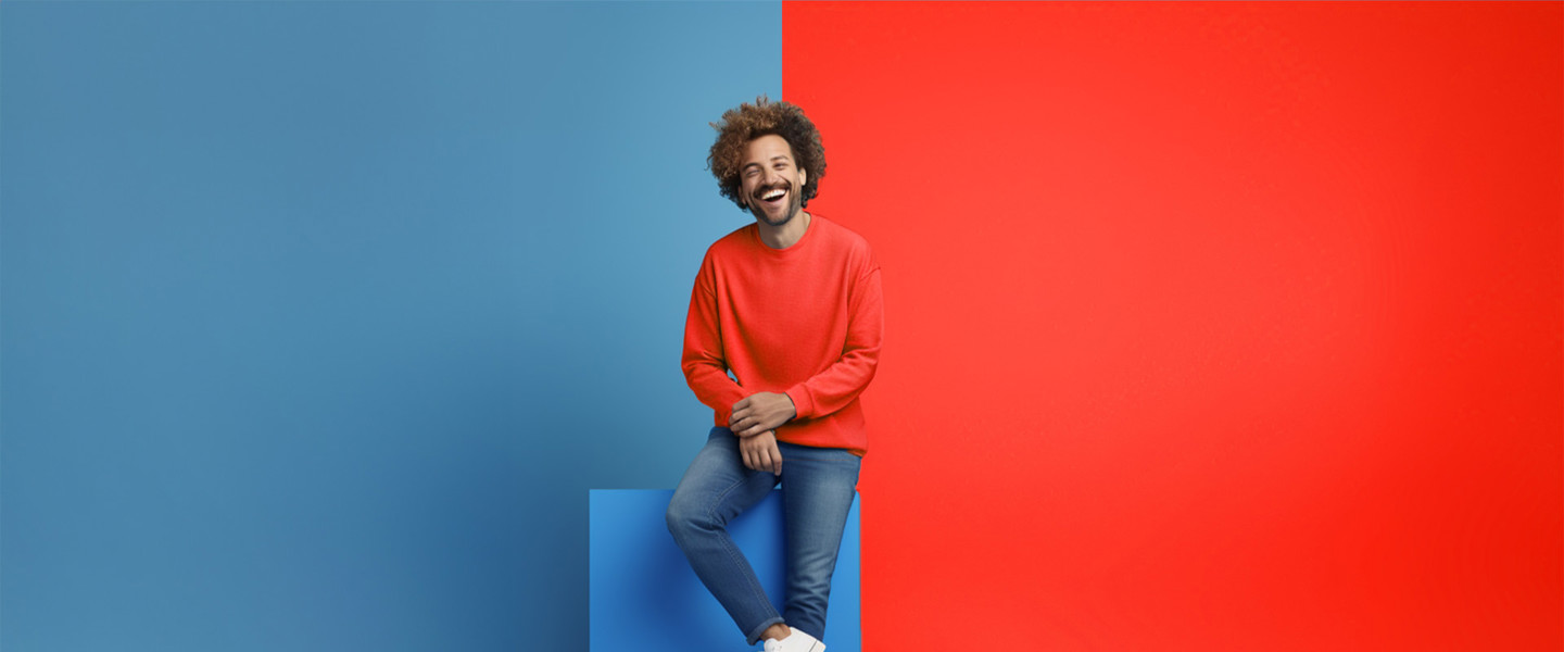 Persoon in rode trui en spijkerbroek staat op een blauw blok, omringd door een blauwe en een rode achtergrond.