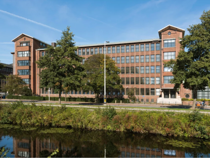 A five-story brick office building with large windows, surrounded by trees and reflecting in the water.