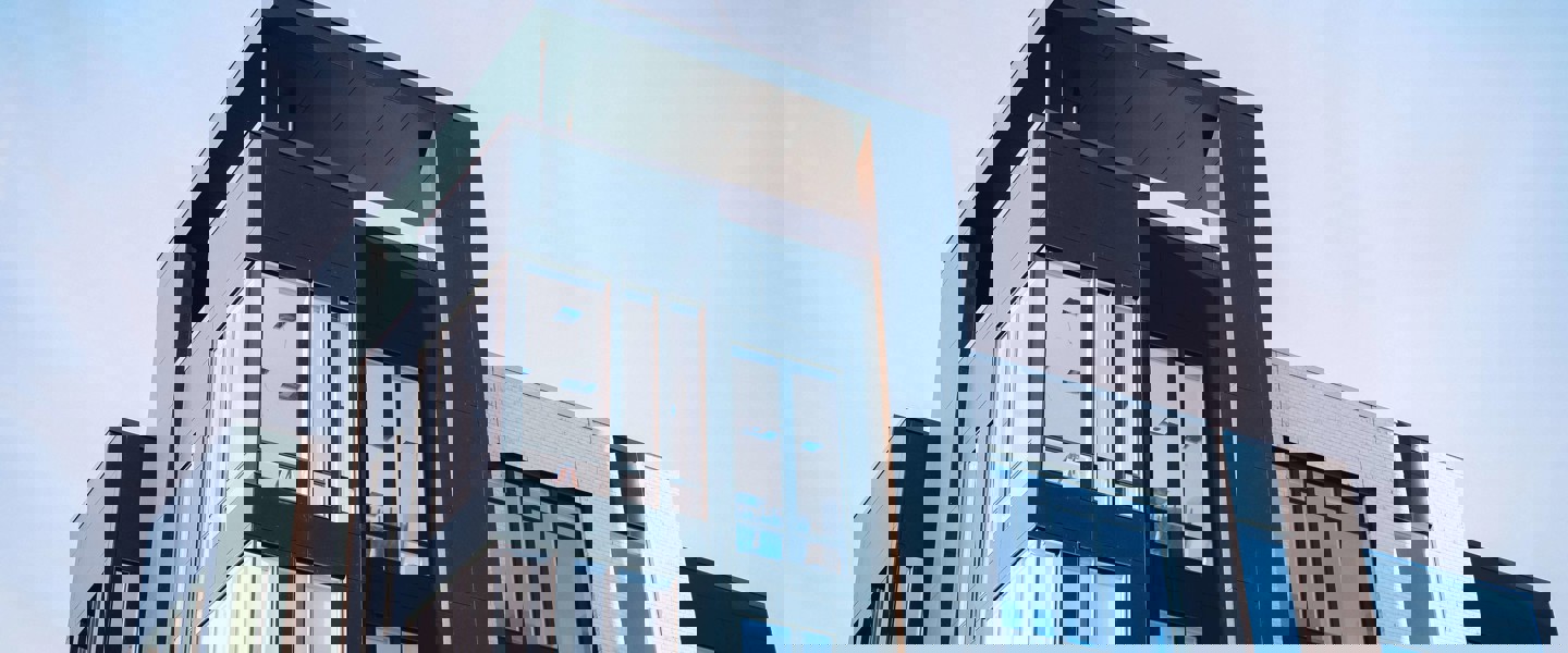 Moderne appartementencomplex met grote ramen en een strakke, donkergekleurde gevel, tegen een heldere blauwe lucht.