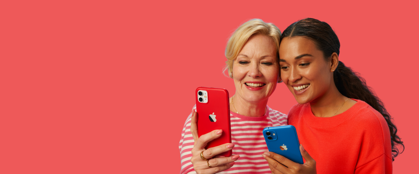 Twee vrouwen in kleurrijke kleding kijken samen naar de schermen van hun smartphones die in verschillende kleuren zijn.