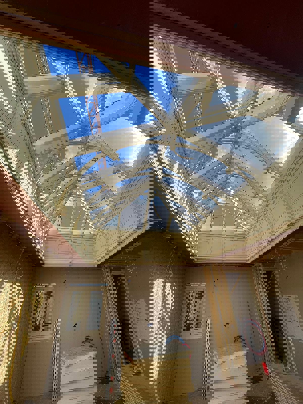 Interieur van een gebouw met een grote glazen koepel en houten spanten, onder een heldere blauwe lucht.