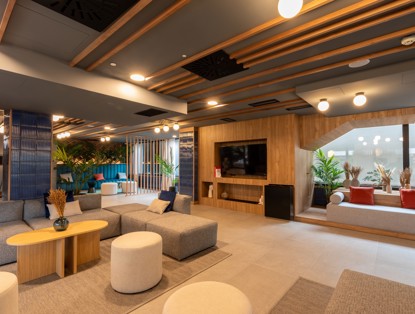 Modern lounge area with comfortable seating, plants, and a large television mounted on a wooden wall.