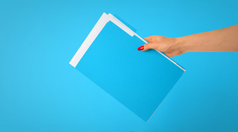 Een hand houdt een stapel blauwe mappen voor een heldere blauwe achtergrond.