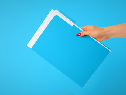 Een hand houdt een stapel blauwe mappen voor een heldere blauwe achtergrond.