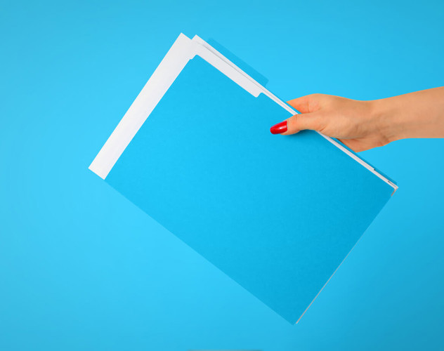Een hand houdt een stapel blauwe mappen voor een heldere blauwe achtergrond.