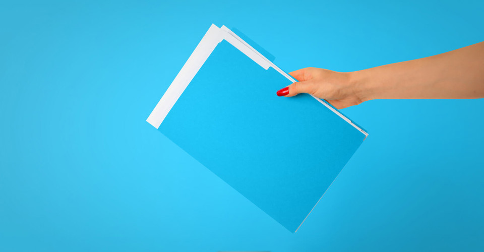 Een hand houdt een stapel blauwe mappen voor een heldere blauwe achtergrond.