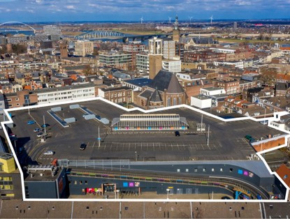 Aerial view of a parking lot with empty spaces, surrounded by urban buildings and a water view in the background.