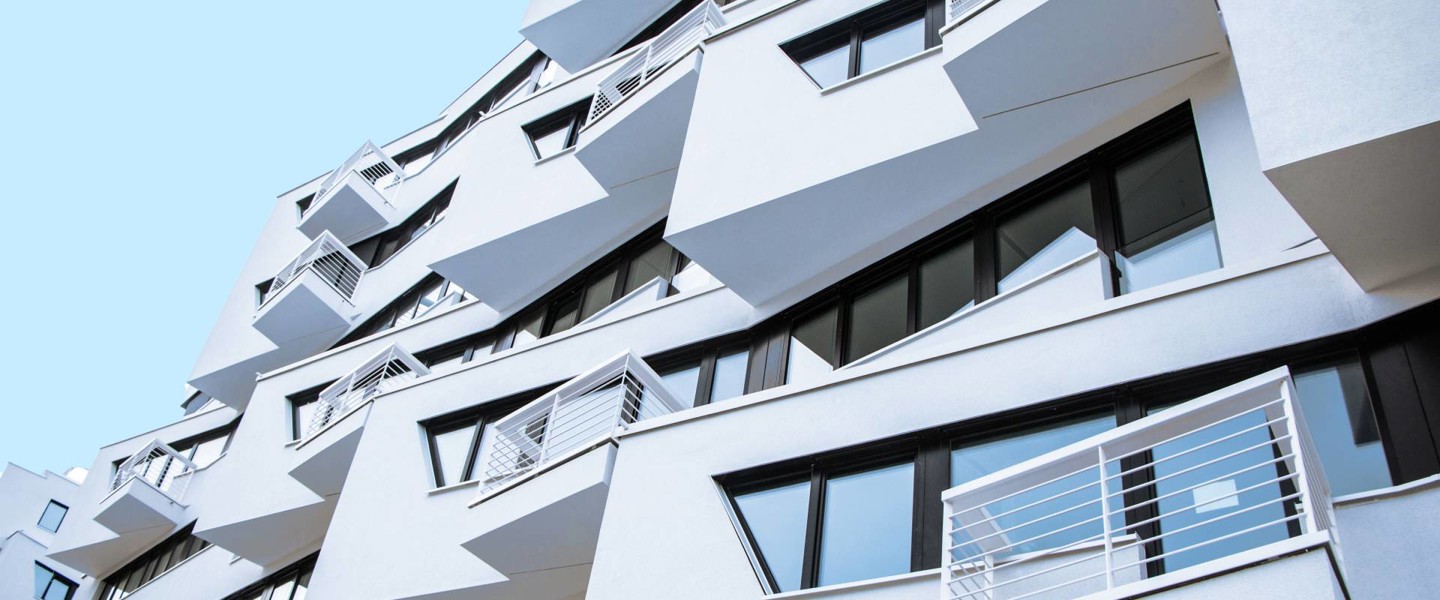 Modern house with distinctive slanted balconies and many large windows against a bright blue sky.