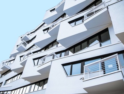 Modern house with distinctive slanted balconies and many large windows against a bright blue sky.