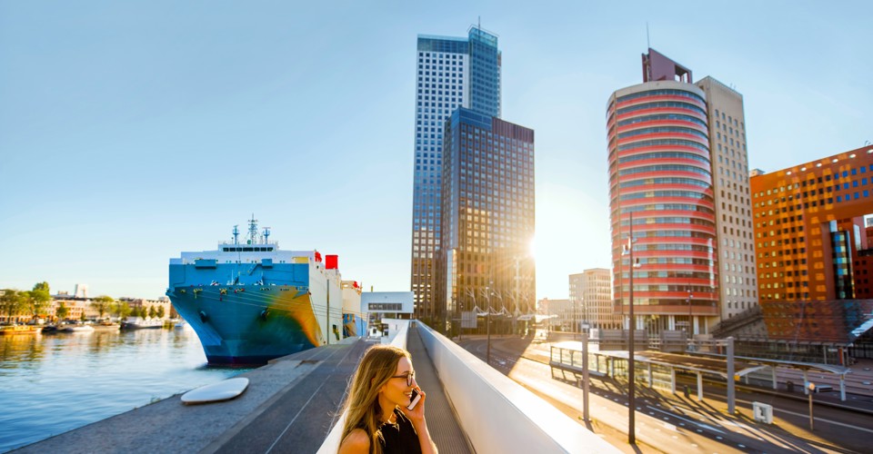 Urban view of a harbor with a large ship and modern buildings in the background, illuminated by the sunset.