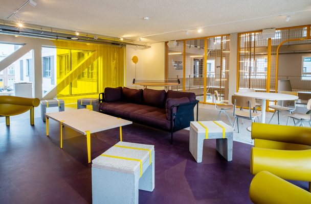 Moderne, lichte ruimte met een paarse vloer en gele accenten, ingericht met een paarse bank, een lichte tafel en betonnen meubels.