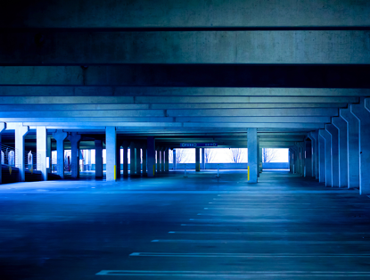 Empty parking lot with concrete pillars and blue lighting, identifiable by the vacant parking spaces.