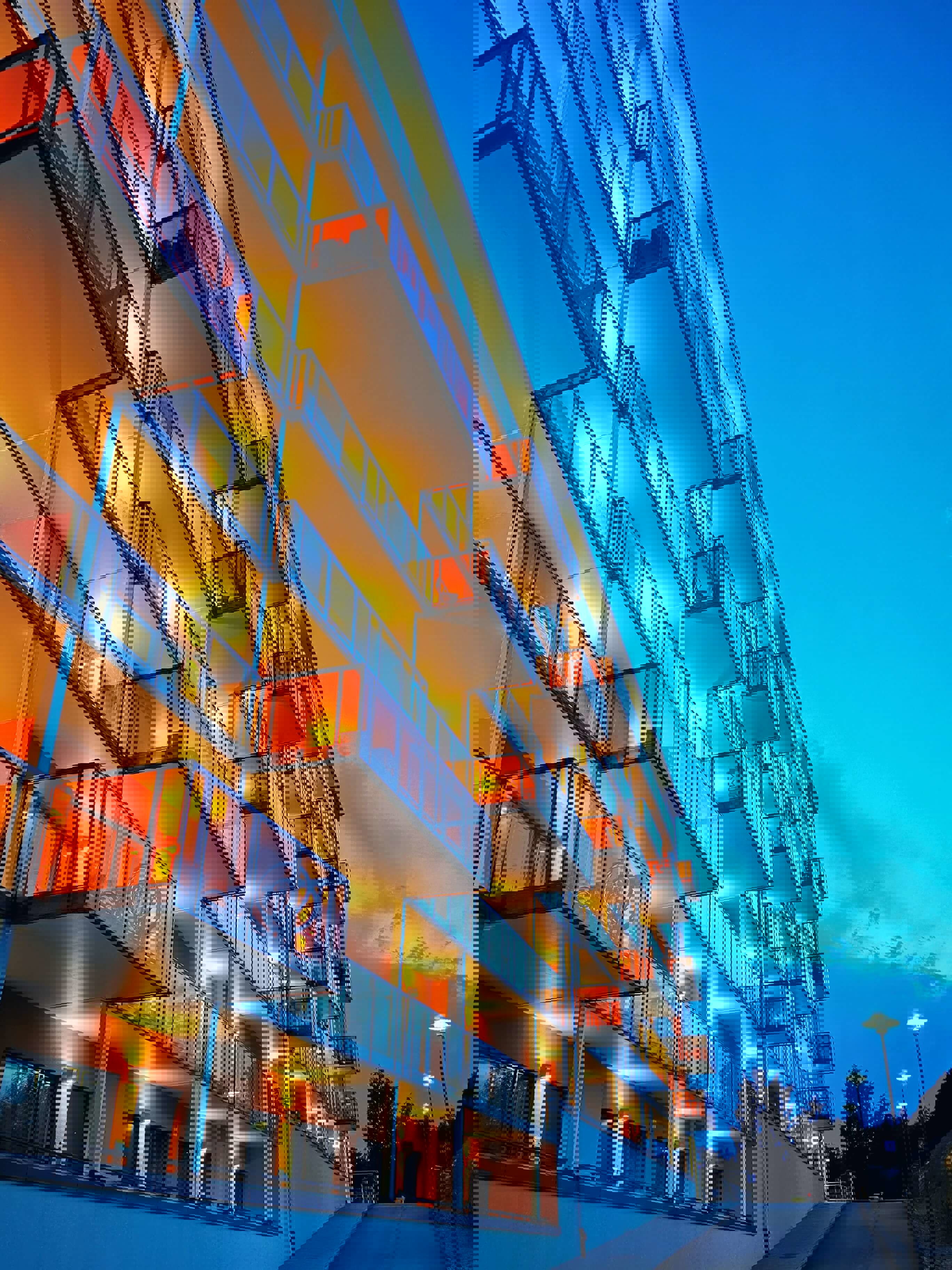 Moderne appartementsgebouwen met verlichte balkons in de avondlucht onder een heldere blauwe hemel.