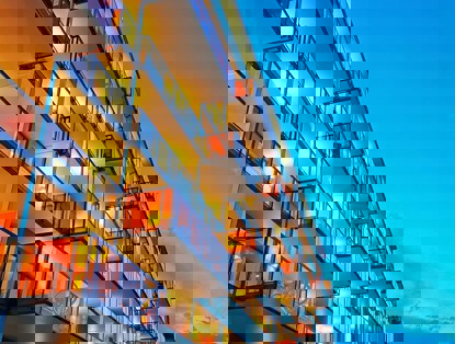 Moderne appartementsgebouwen met verlichte balkons in de avondlucht onder een heldere blauwe hemel.