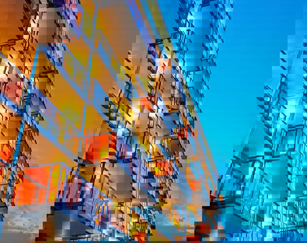 Moderne appartementsgebouwen met verlichte balkons in de avondlucht onder een heldere blauwe hemel.