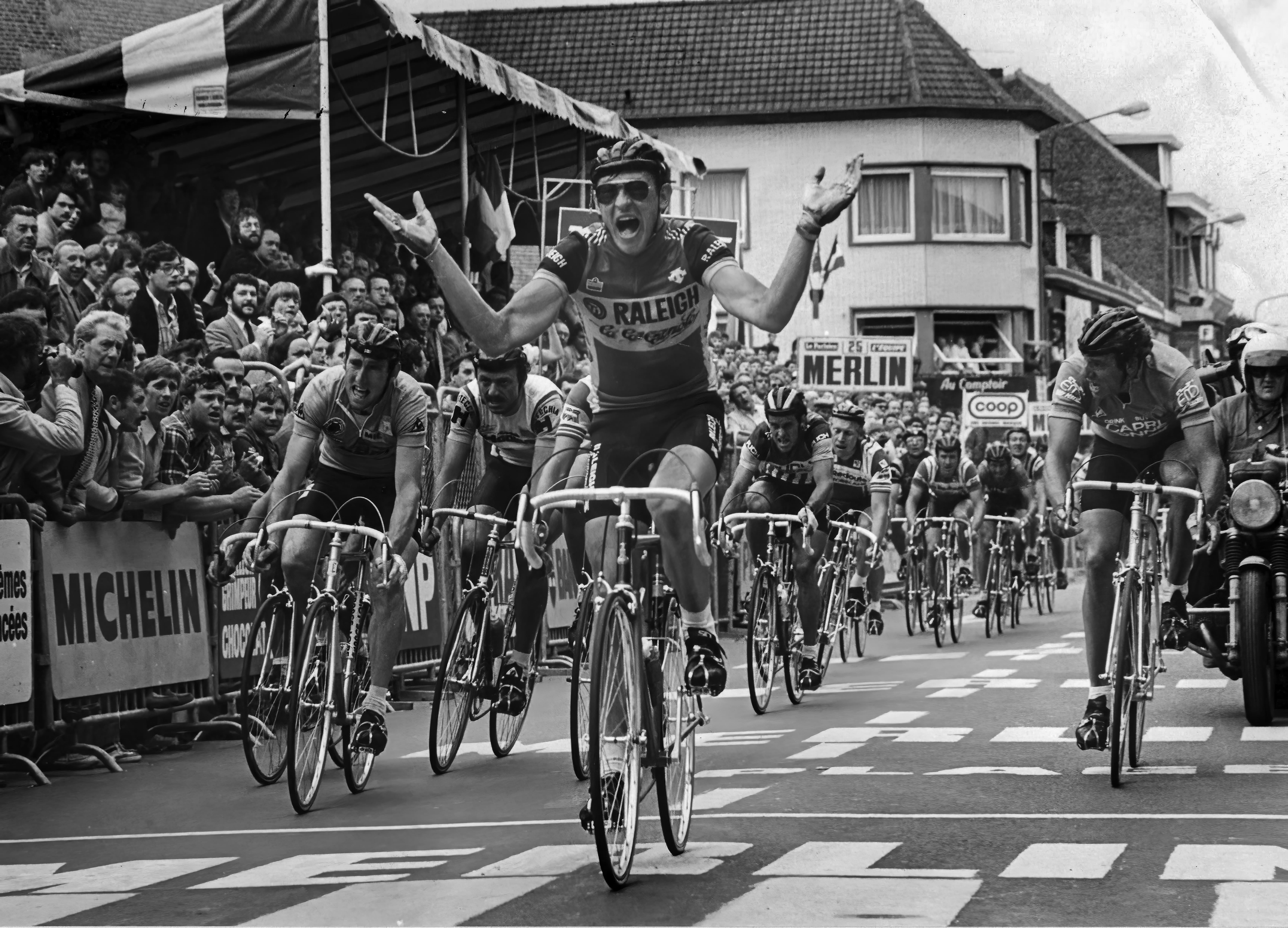 Fietsers vieren hun overwinning in een wielerwedstrijd, omringd door juichende fans en sponsoren.