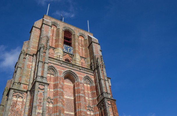 Vogelperspectief van een historische toren met een klok, tegen een achtergrond van een blauwe lucht.