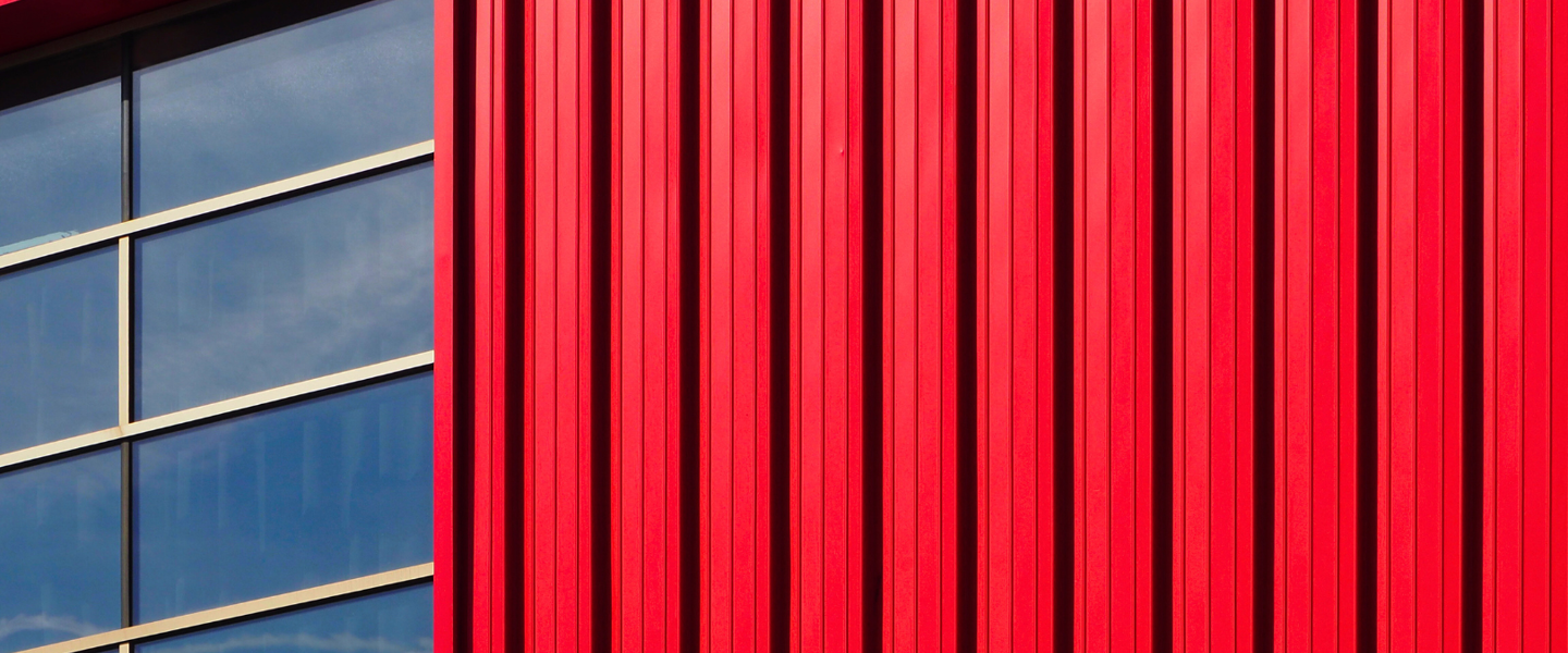 Red-paneled metal wall with a large window reflecting a blue sky.
