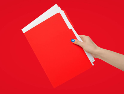 Hand die een stapel rode mappen vasthoudt tegen een heldere rode achtergrond.