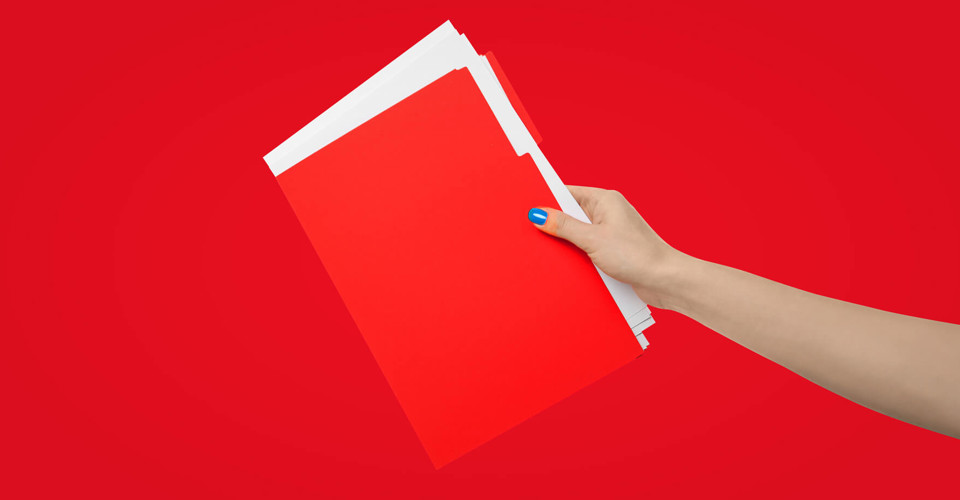 Hand die een stapel rode mappen vasthoudt tegen een heldere rode achtergrond.