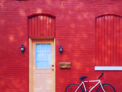 Rode bakstenen muur met een lichte deur en een fiets aan de rechterzijde.