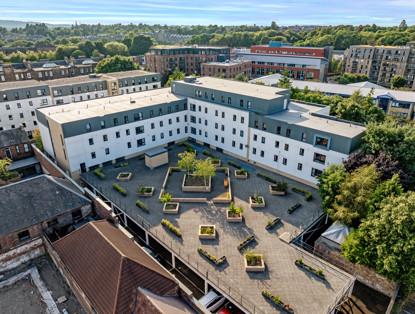 Aerial photo of a modern residential complex featuring a central courtyard filled with plants and benches, surrounded by buildings and trees.