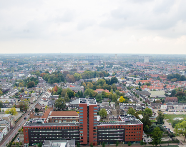 Panoramisch uitzicht op een stedelijk landschap met gebouwen, groen en een bewolkte lucht.