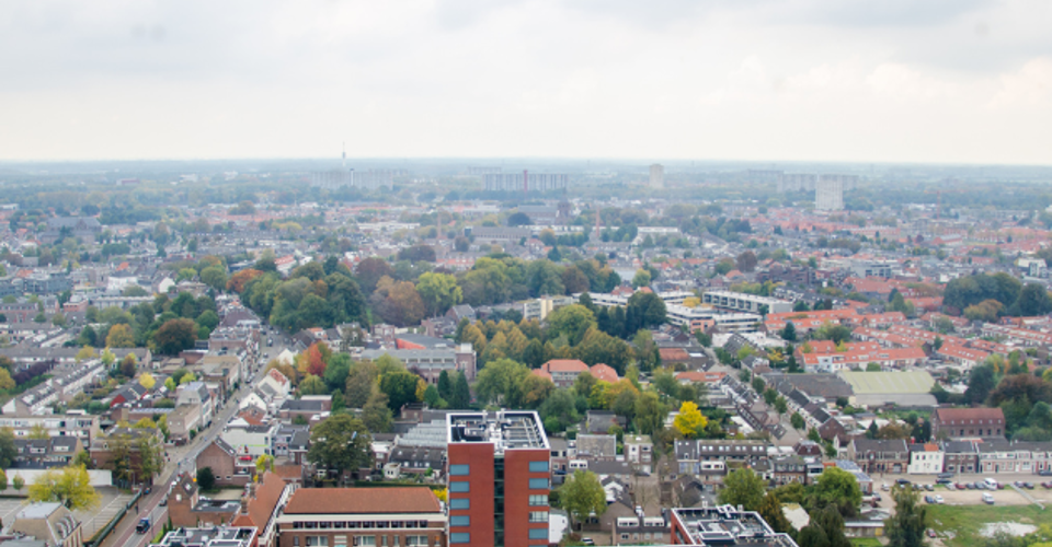 Panoramisch uitzicht op een stedelijk landschap met gebouwen, groen en een bewolkte lucht.