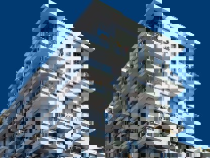 Modern appartementencomplex met meerdere verdiepingen en balkons, tegen een heldere blauwe lucht.