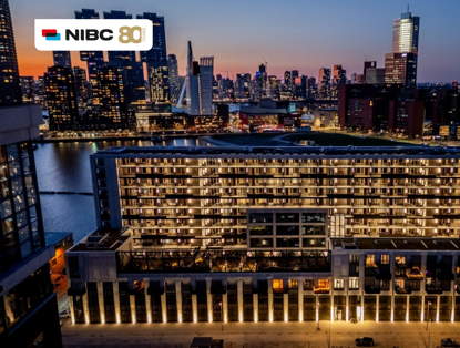 Cityscape of a lit skyline featuring modern buildings and water, with an NIBC 80 year logo at the top.