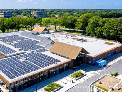 Aerial view of a modern, sustainable building with solar panels on the roof, surrounded by greenery.