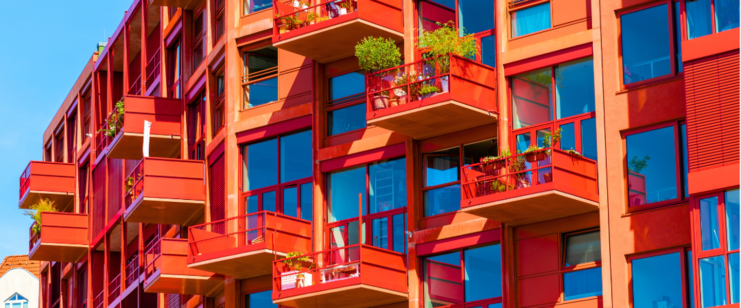 Modern red apartments with glass balconies, each surrounded by greenery.