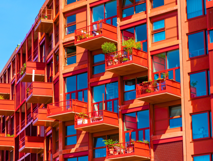 Modern red apartments with glass balconies, each surrounded by greenery.
