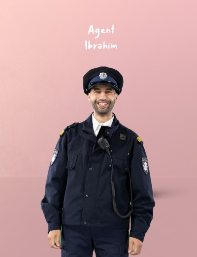 Agent Ibrahim in uniform met politiepet en microfoon, tegen een roze achtergrond.